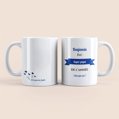 Mug blanc. Texte et banderole personnalisés avec nom bleu à droite. Etoiles plus texte personnalisé avec nom à gauche.